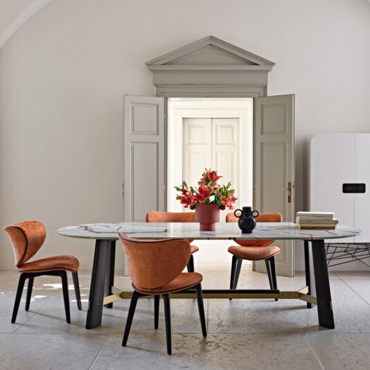 Mid Century Style Dining Chair A contemporary dining room featuring a marble-top table with black legs. The table is surrounded by four cushioned Mid Century Style Dining Chairs in orange, each with elegantly curved backs. At the center of the table sits a vibrant red flower arrangement. Double doors and a sleek white cabinet serve as the background.