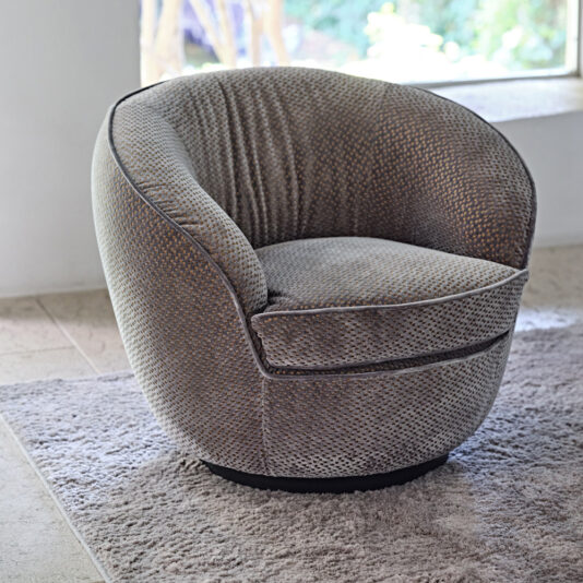 Modern Luxury Swivel Armchair A **Modern Luxury Swivel Armchair** with a textured fabric surface is placed on a light gray rug. The chair is positioned near a large window that lets in natural light, and the background features a neutral-toned floor and a blurred outdoor view.