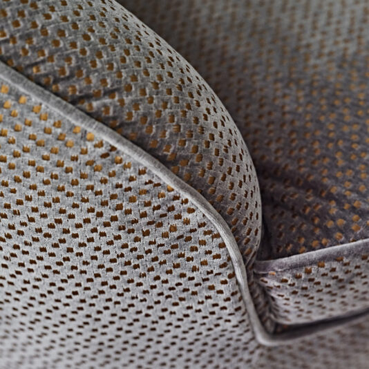 Modern Luxury Swivel Armchair Close-up of the Modern Luxury Swivel Armchair, upholstered in grey fabric adorned with a small, uniform pattern of golden dots. The image captures the chair's seam and contours, emphasizing the texture and intricate detail of the upholstery.