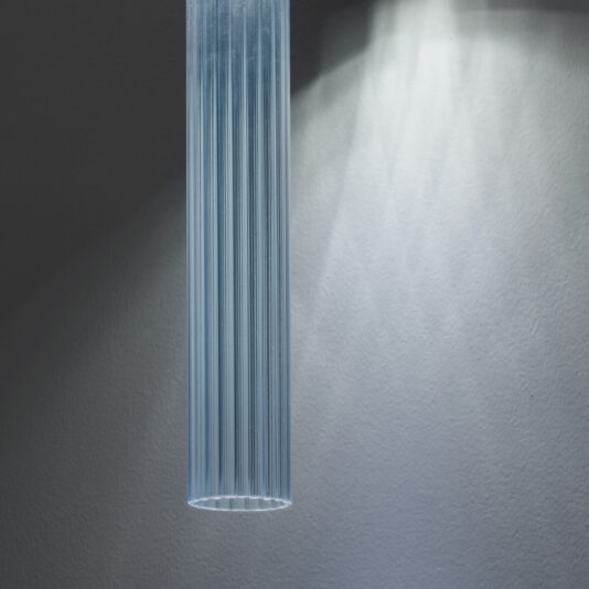 A close-up shot of the Contemporary Vertical Glass Tube Wall Light, softly illuminating the textured wall behind it. The fixture features linear detailing and emits a cool-toned glow.