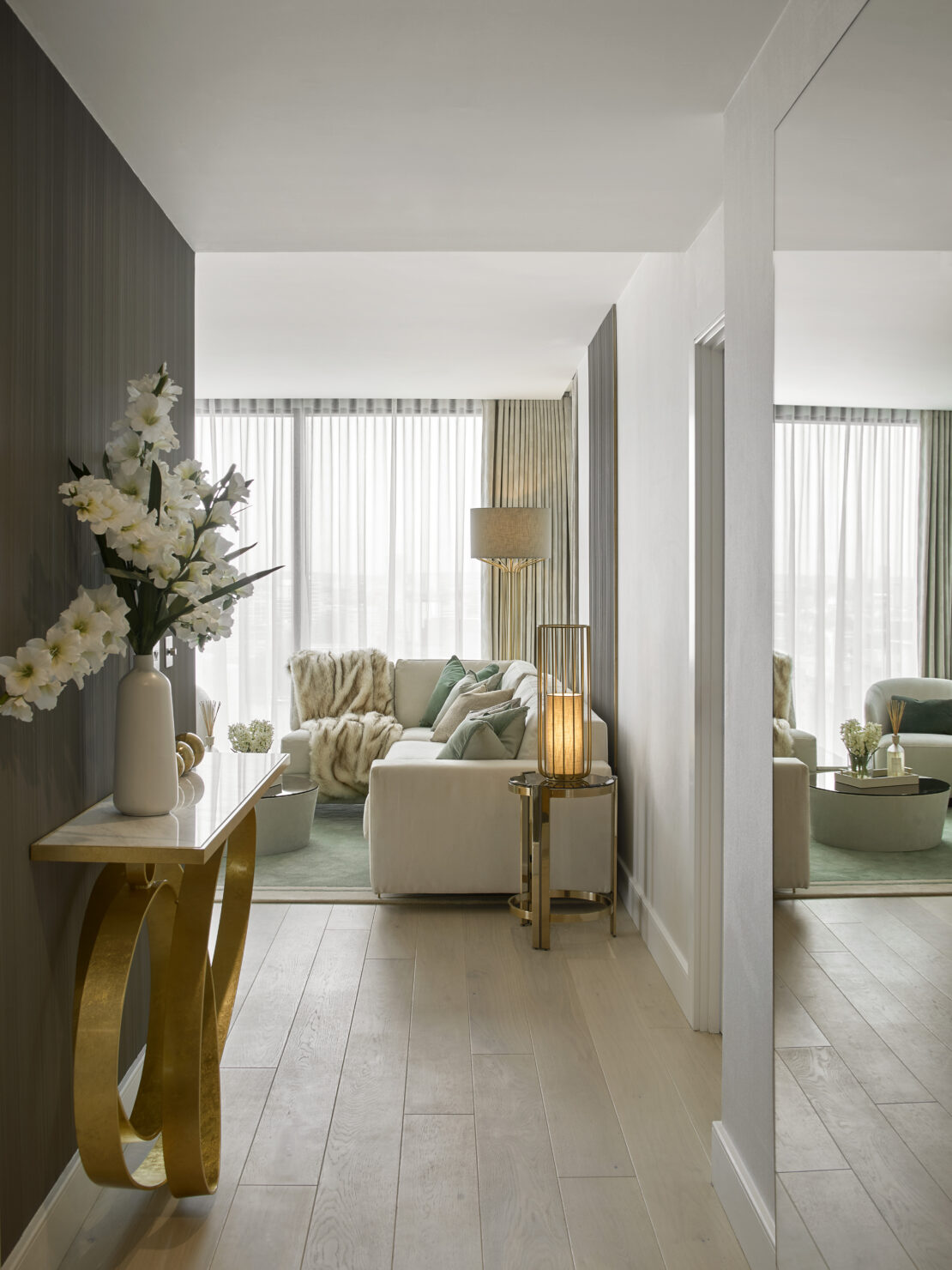 Luxury apartment hallway, light airy and elegant feeling with gold console table, large mirror leading to a luxury living room with white and green accents