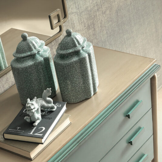 Luxury Art Deco Style Chest Of Drawers A stylish Luxury Art Deco Style Chest of Drawers with a light-colored wooden top and pastel green body features two textured green ceramic jars with pointed lids and a small decorative horse sculpture, along with the book