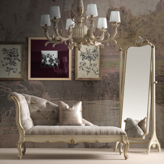 Rococo Style Chaise Longue A luxurious interior showcasing a vintage chaise lounge with ornate detailing, a Rococo Style Wall Mirror, framed botanical art adorning the wall, and an elegant chandelier with multiple lights. This setting exudes a classic, sophisticated ambiance.