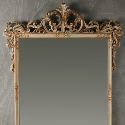 Large Baroque Style Wall Mirror The Large Baroque Style Wall Mirror features an ornate antique-style design with a beautifully intricate carved wooden frame, enhanced by decorative scrollwork and floral motifs at the top. It is displayed against a textured wall adorned with subtle artistic patterns.