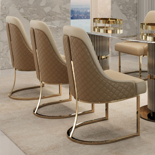 Three Modern Two-Tone Dining Chairs in elegant beige and brown with quilted backs and gold legs surround a table with gold accents. They sit on a light carpet, against marble walls, framing a window showcasing a stunning city view.