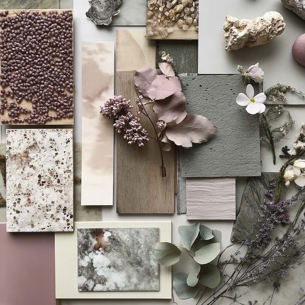 A flat lay of various textures and materials showcases floral arrangements, fabric swatches, and textured sample tiles. The color scheme, featuring muted pinks, greens, and neutrals, is complemented by the rich tone of Mocha Mousse. Natural elements like leaves and flowers add a soft, organic touch.