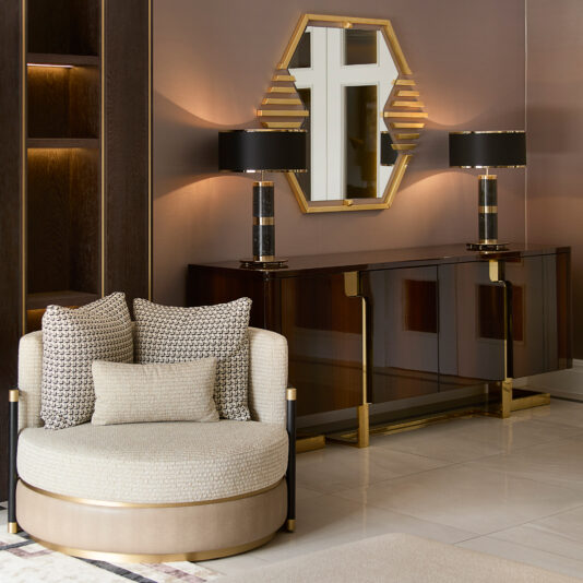 Art Deco Inspired Hexagonal Mirror Luxurious living room with a circular beige chair and patterned cushions, a gold-accented wooden sideboard adorned with matching black and gold lamps, topped by the Art Deco Inspired Hexagonal Mirror that enhances ambient light.