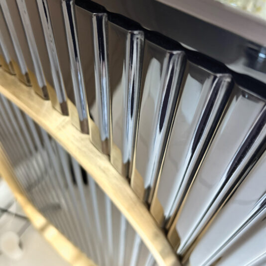 Close-up of shiny metal bars in a curved wooden frame, reflecting light and mirroring the refined, modern look of the Luxury Art Deco Style Sunburst Sideboard. The design captures classic elegance with a contemporary twist.