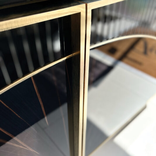 Close-up of the Luxury Art Deco Style Sunburst Sideboard in black and gold, showcasing reflective surfaces, sharp lines, and a modern sunburst design with sunlight casting dramatic shadows.
