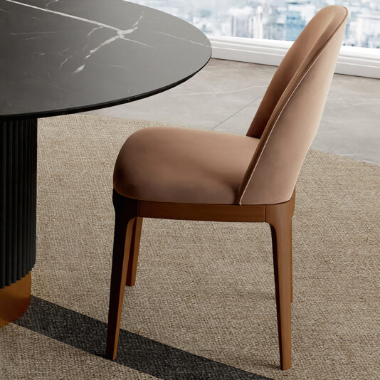 Modern Dining Chair The Modern Dining Chair, upholstered in light brown fabric with wooden legs, is placed next to a round stone-effect dining table on a beige carpet, set beside a large window.