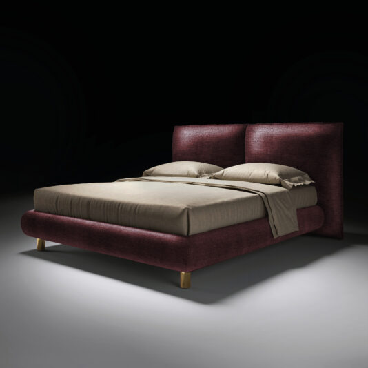 The Contemporary Italian Bed features a dark burgundy upholstered frame and headboard, beige bedding with two pillows, and wooden legs, all showcased against a plain black background with dramatic lighting.