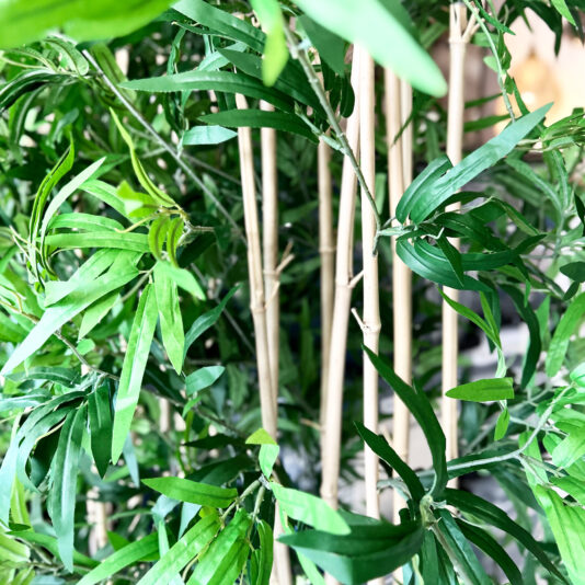 Close-up of thin bamboo stems and lush, narrow green leaves, accented by the elegant Faux White Agapanthus in Glazed Bowl (Copy) nestled among the vibrant foliage.