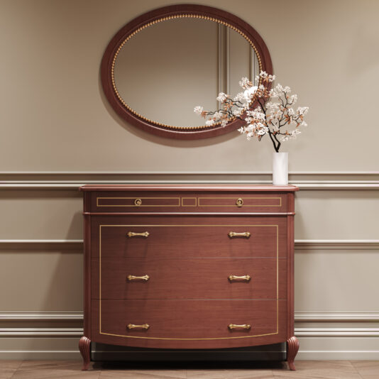 The Classic Style Cherrywood Chest of Drawers with gold handles rests against a beige wall with skirting, topped by a white vase with blooming branches. Above it, a round mirror completes the elegant arrangement.